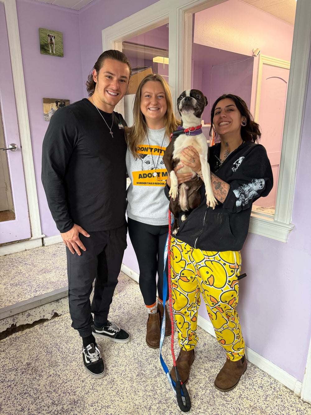 Three people in a lavender shelter lobby, one holding a black and white dog.