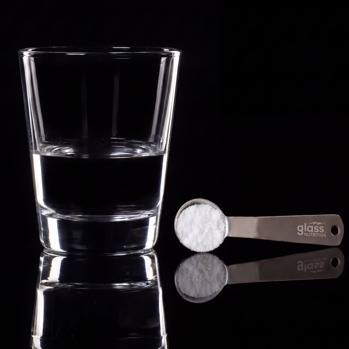A glass of water beside a Glass Nutrition steel scoop filled with creatine powder