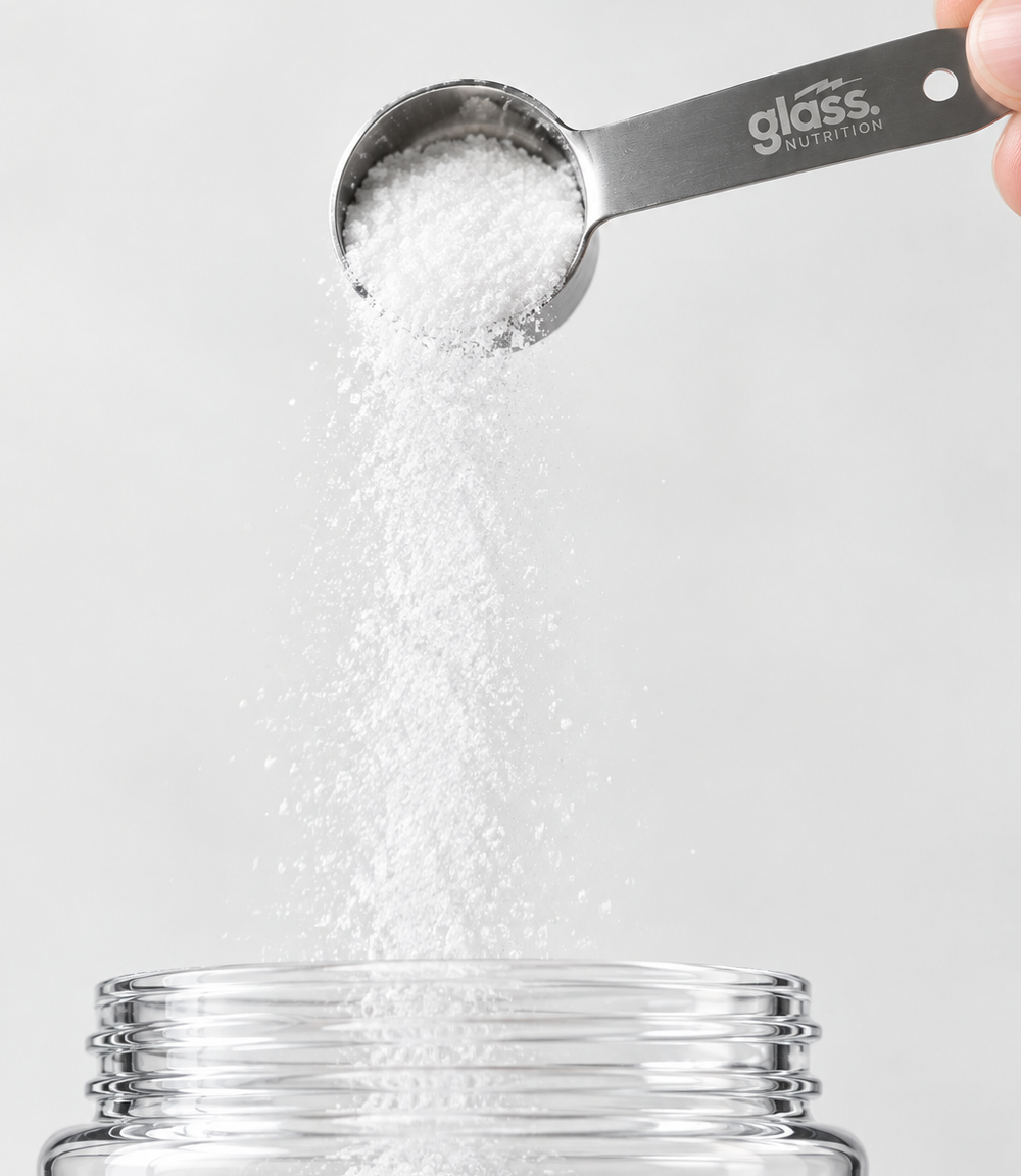 A hand holding a Glass Nutrition steel scoop and pouring creatine powder