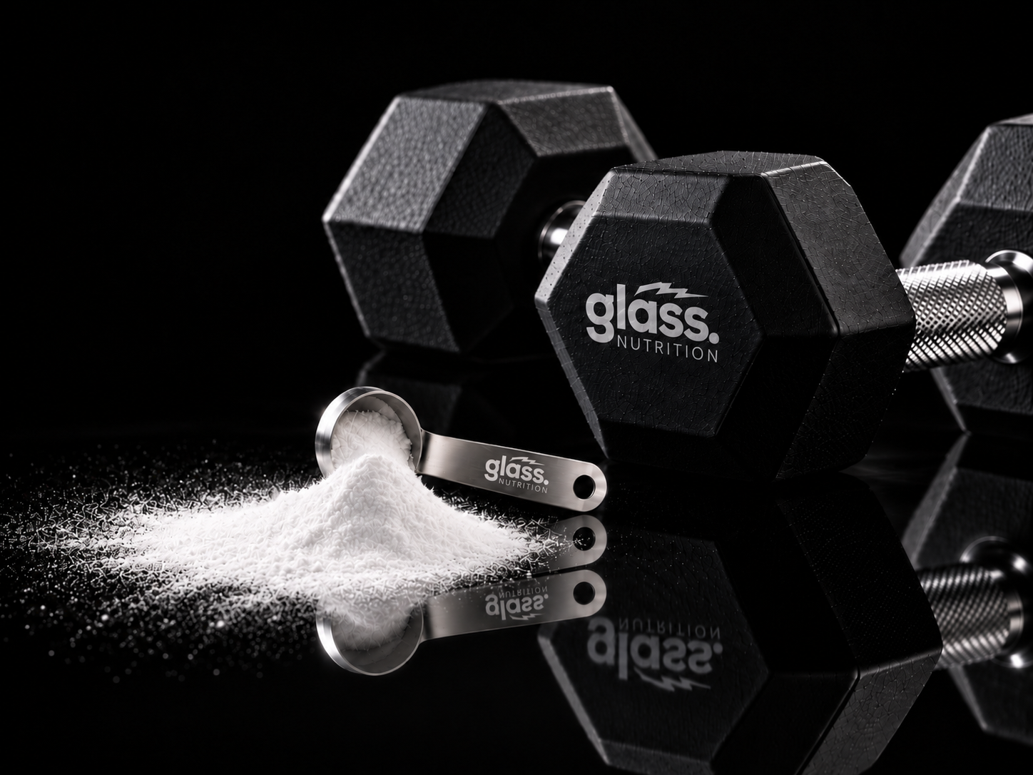 A Glass Nutrition dumbbell beside a steel scoop and a pile of creatine powder on a black surface