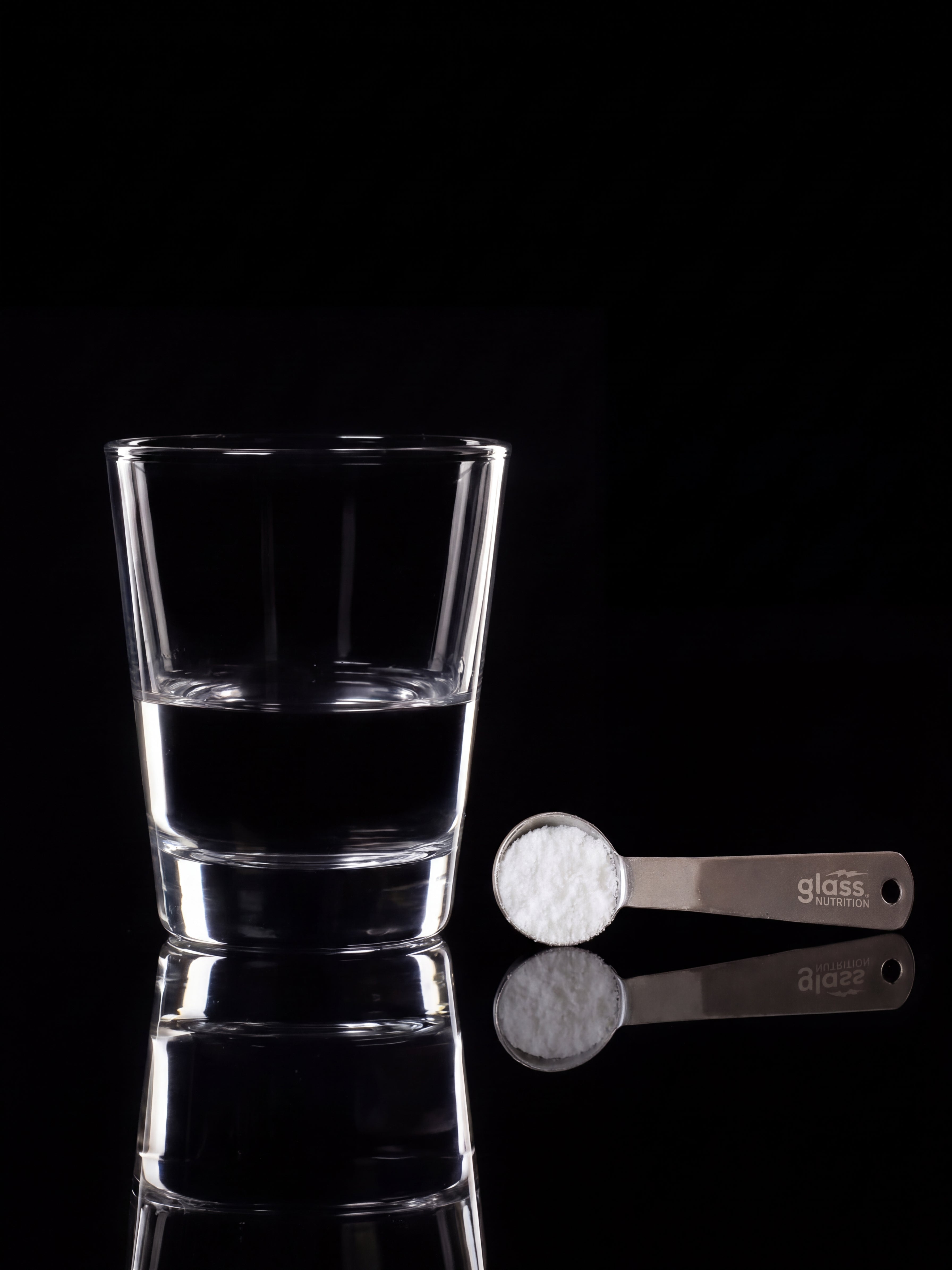 A glass of water beside a Glass Nutrition steel scoop filled with creatine powder