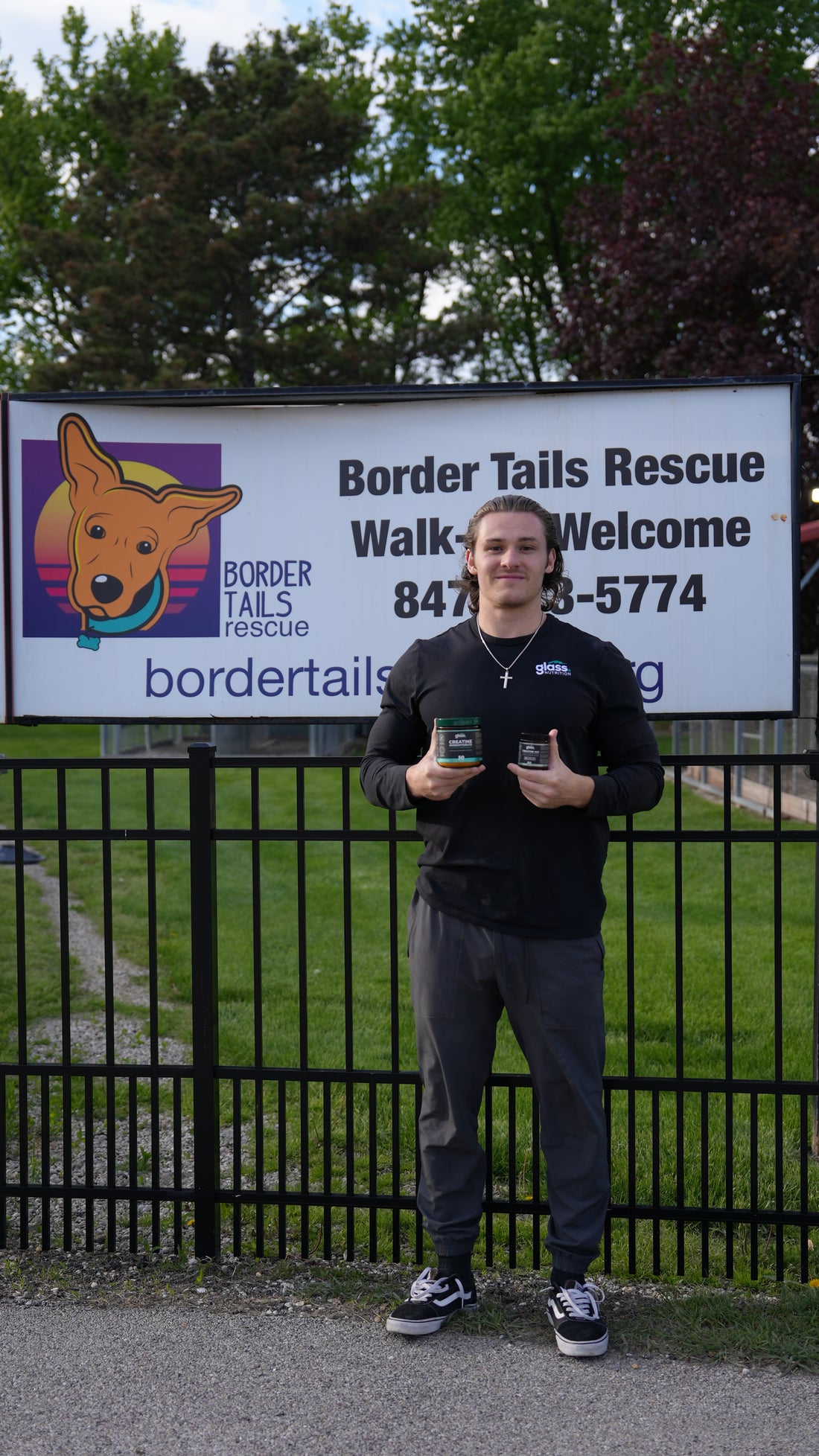 The founder holding jars of Glass Nutrition creatine in front of the Border Tails Rescue sign.