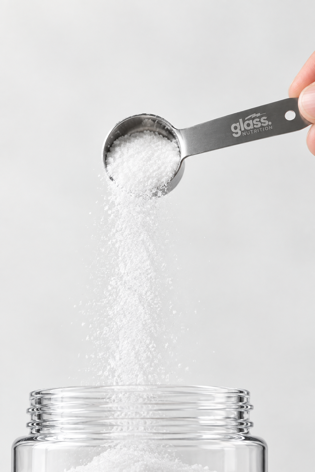 A hand holding a Glass Nutrition steel scoop and pouring creatine powder
